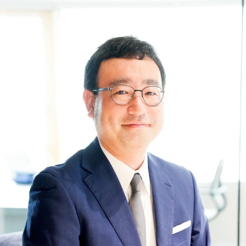 青いスーツと眼鏡をかけたアジア系の男性