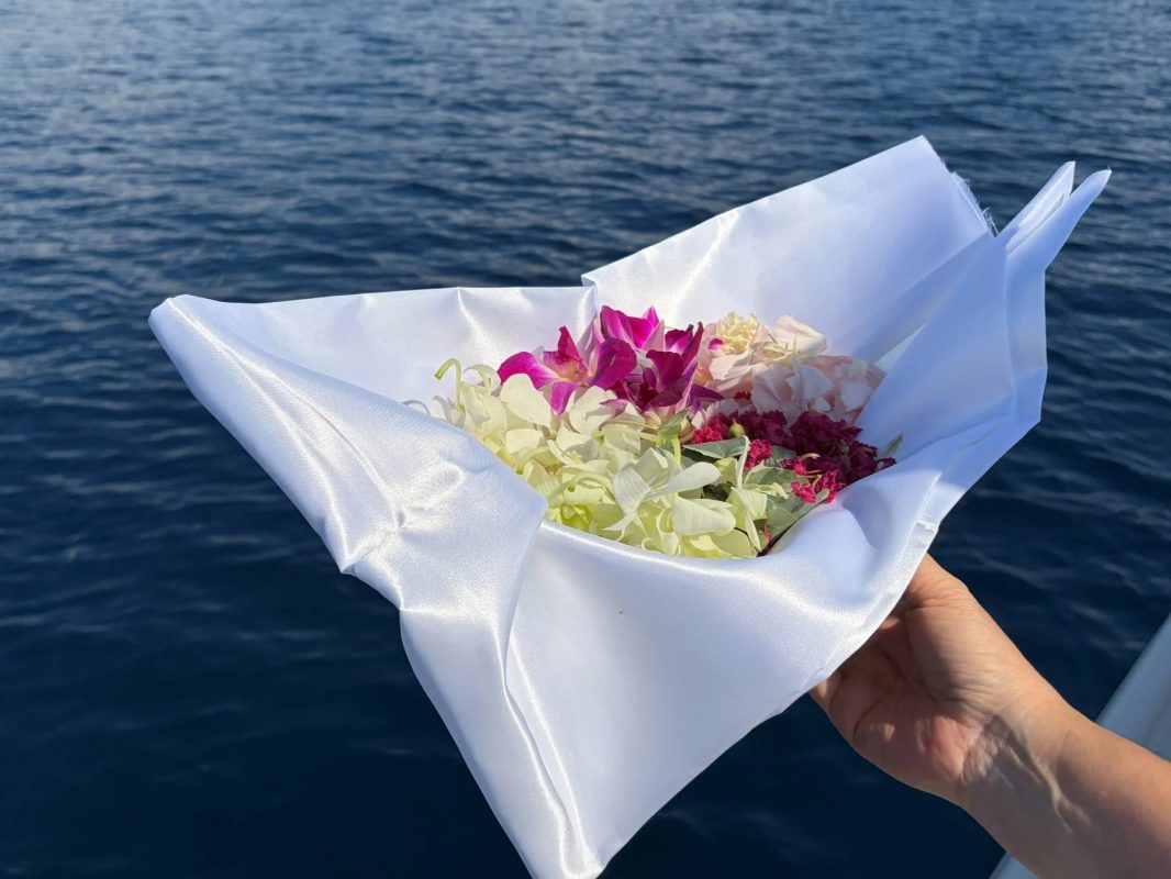 青い海を背景に、白い布に包まれた色とりどりの花束を持つ手のクローズアップ