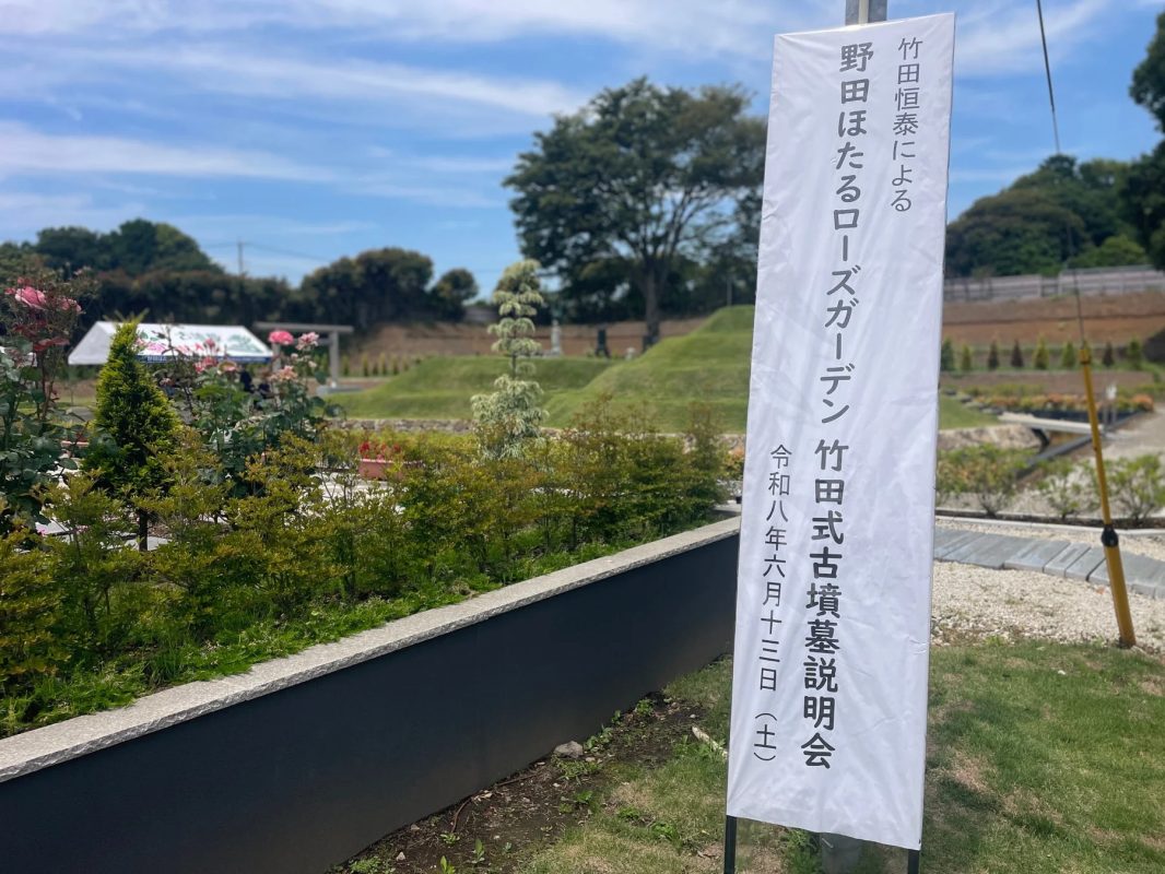 野田ほたるローズガーデンの風景で、竹田恒泰氏による竹田式古墳墓説明会の告知バナーが立てられています。青空の下、緑豊かな庭園が広がっており、説明会は令和8年6月13日（土）に開催される予定です。