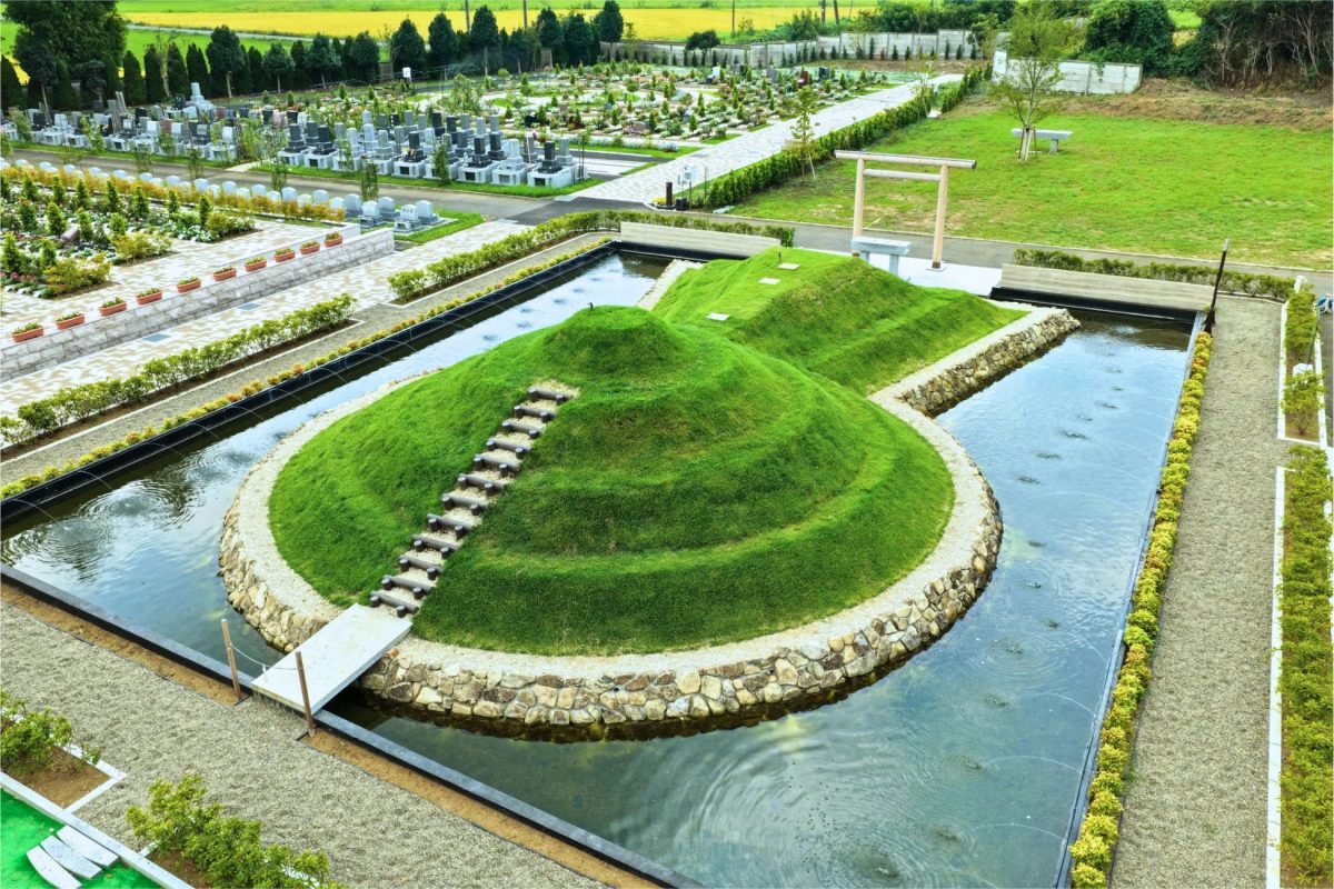 水辺に浮かぶ芝生の丘と鳥居がある霊園の俯瞰景