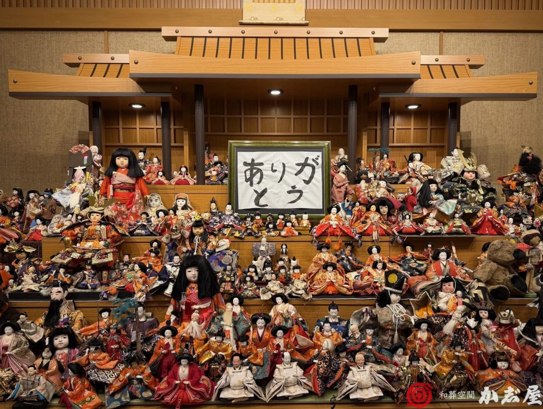 多数の日本人形が多段のひな壇のような形で展示されており、中央には「ありがとう」と書かれた額が飾られています。日本の伝統的な文化や工芸品を感じさせる豪華なディスプレイです。