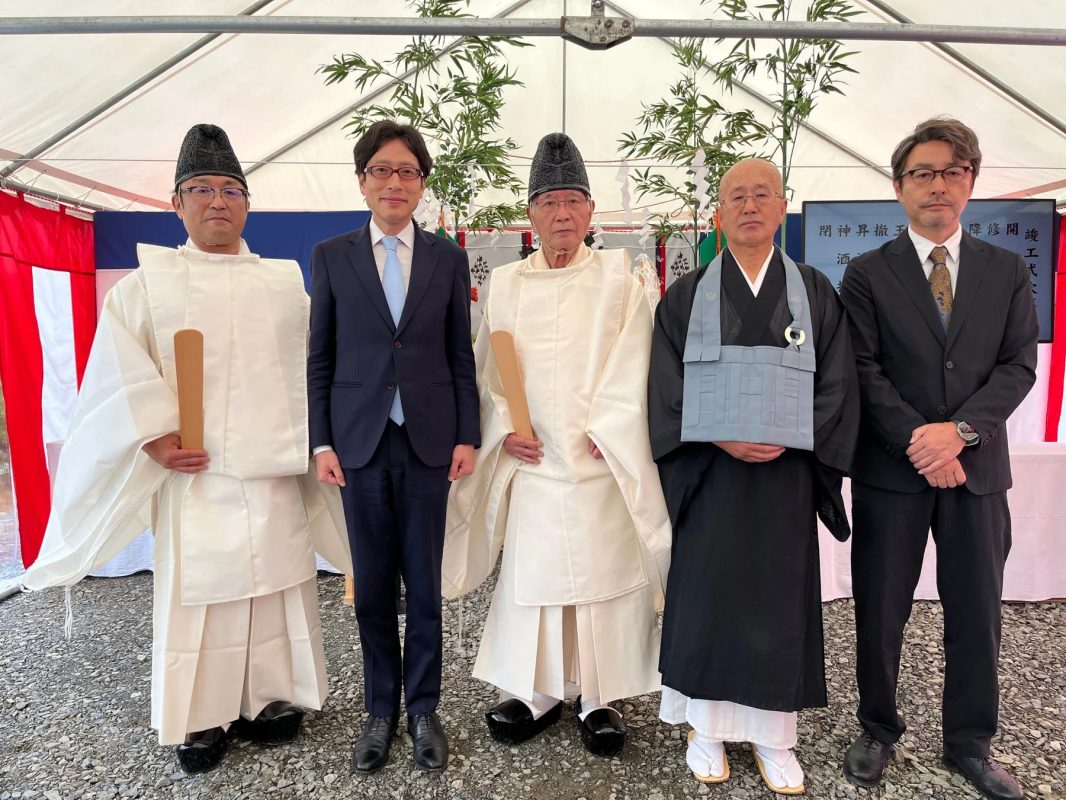 テントの下で、神職、僧侶、スーツ姿の男性5人が並んでおり、竹の装飾や「開山晋山式」「竣工式」の文字が見える。日本の伝統的な式典の様子を捉えた集合写真。