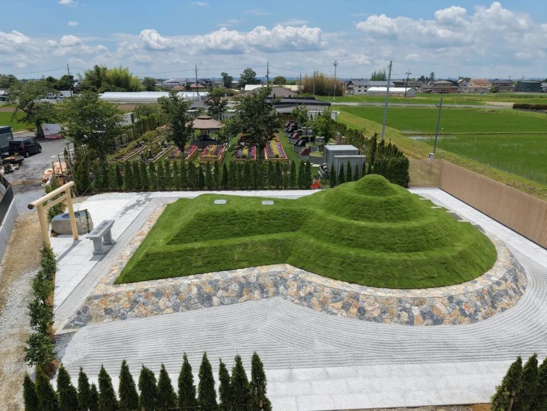 前方後円墳を模した芝生の丘と枯山水が特徴的な霊園の全景。奥には花壇や鳥居が見え、周囲には田園風景が広がる。
