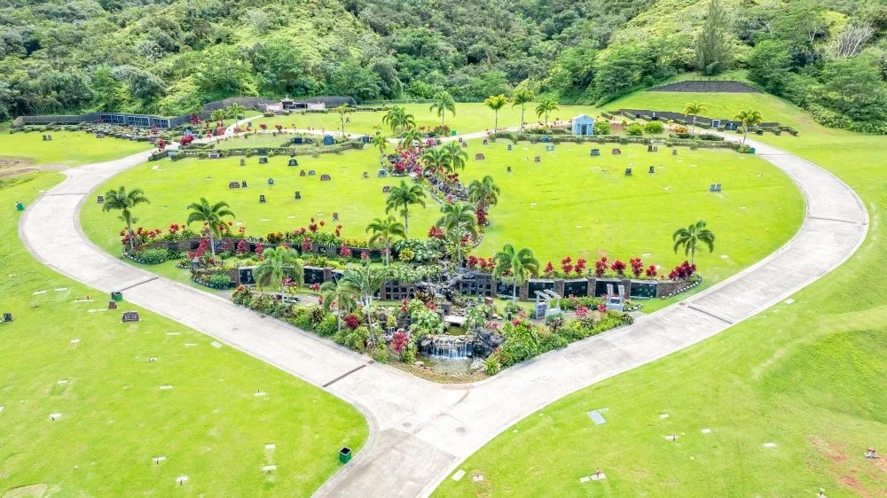 緑豊かな丘陵地にある広大な公園墓地を上空から捉えた画像です。ヤシの木や色鮮やかな花々が植えられ、中央には滝のある美しい庭園があり、安らぎの空間が広がっています。